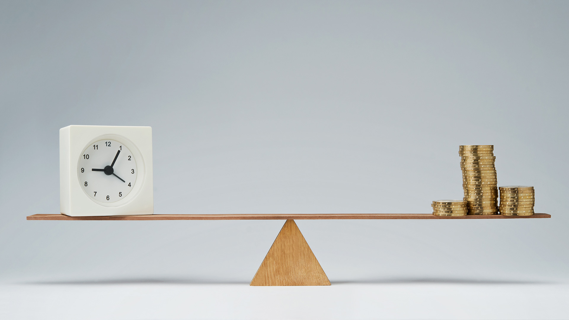 Balancing act with time represented by a clock and money, represented by coins